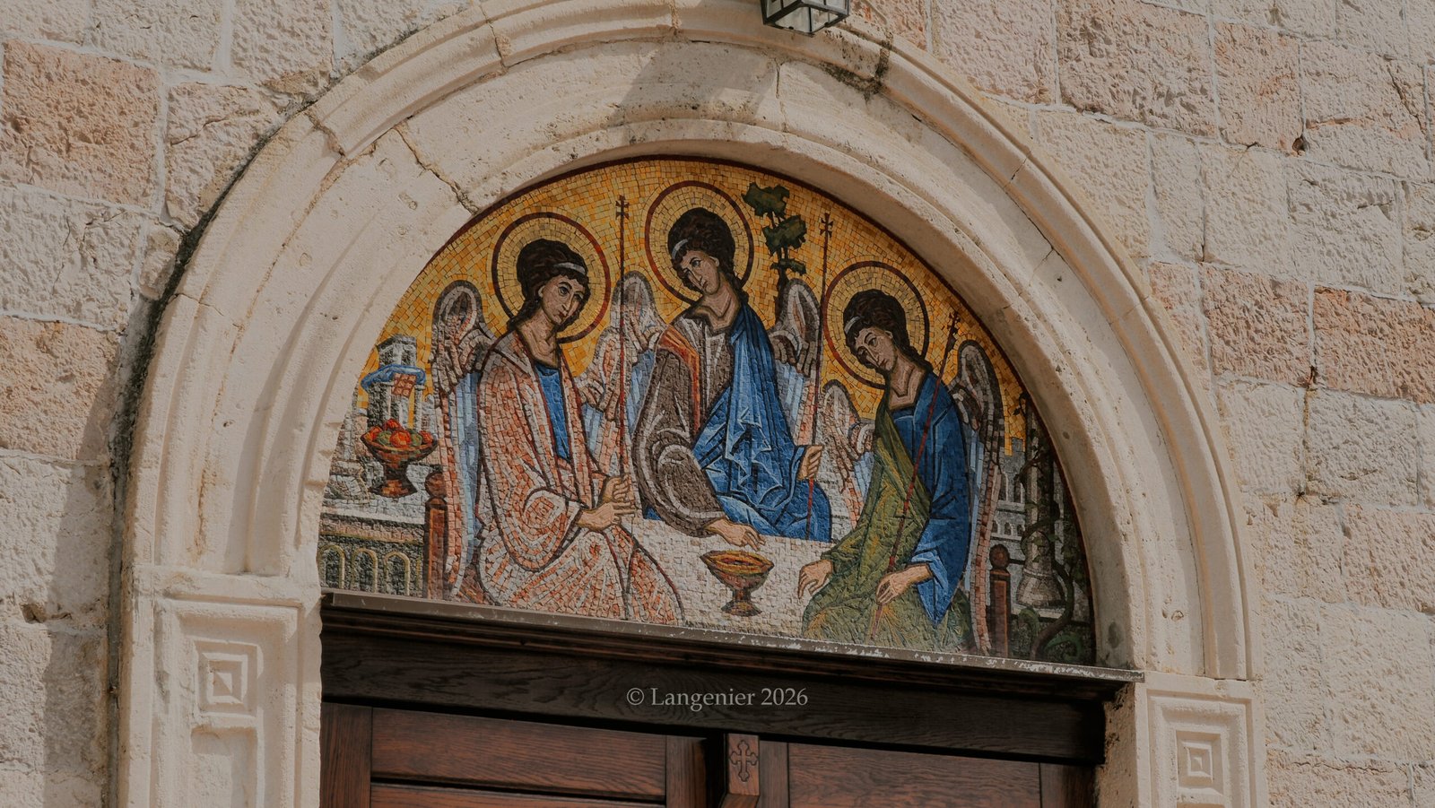 Byzantine-style mosaic of three haloed saints above a church doorway in Budva, Montenegro