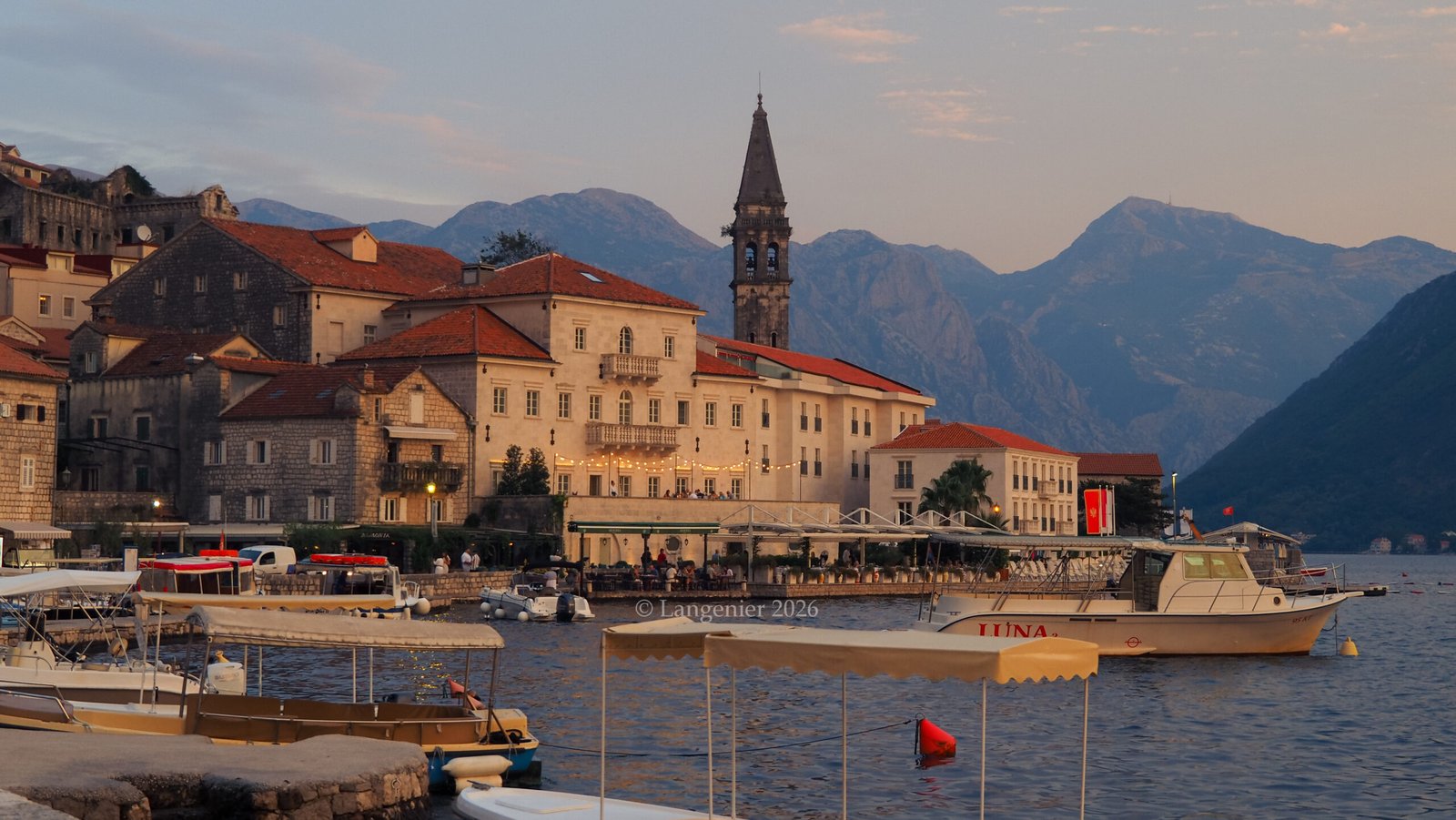 Perast waterfront at sunset with St. Nicholas church bell tower, traditional stone houses and boats, Bay of Kotor, Montenegro