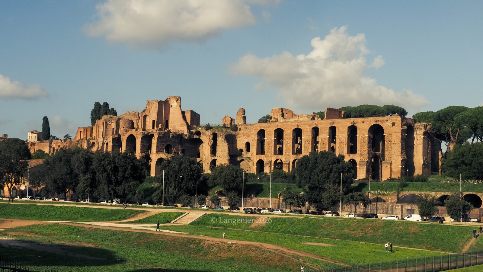 Ancient Roman ruins of the Palatine Hill overlooking the Circus Maximus, with arched brick walls and umbrella pines against a clear blue sky.