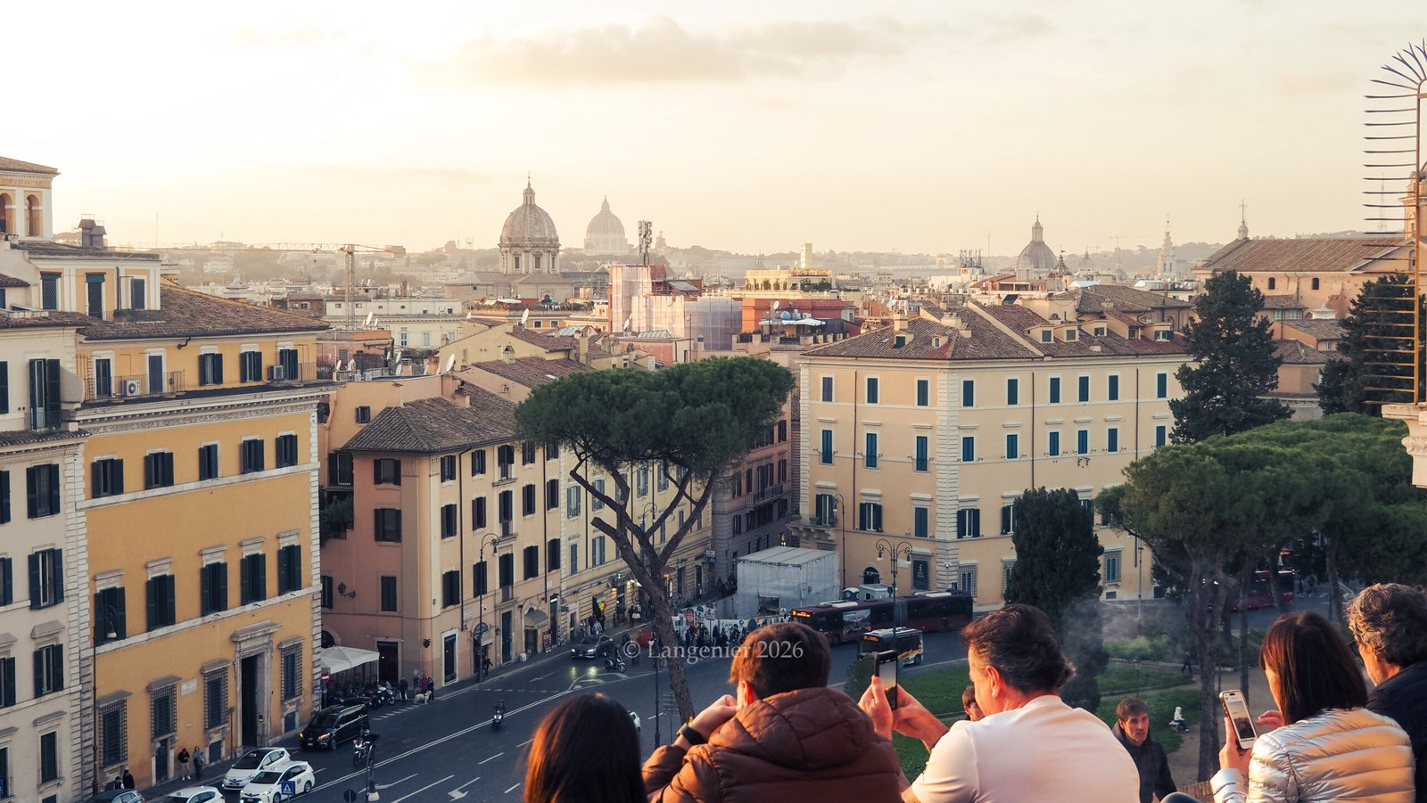 Visitors watching sunset from the terrace of the Basilica di Santa Maria in Aracoeli, overlooking Rome's rooftops toward the domes of St. Peter's Basilica