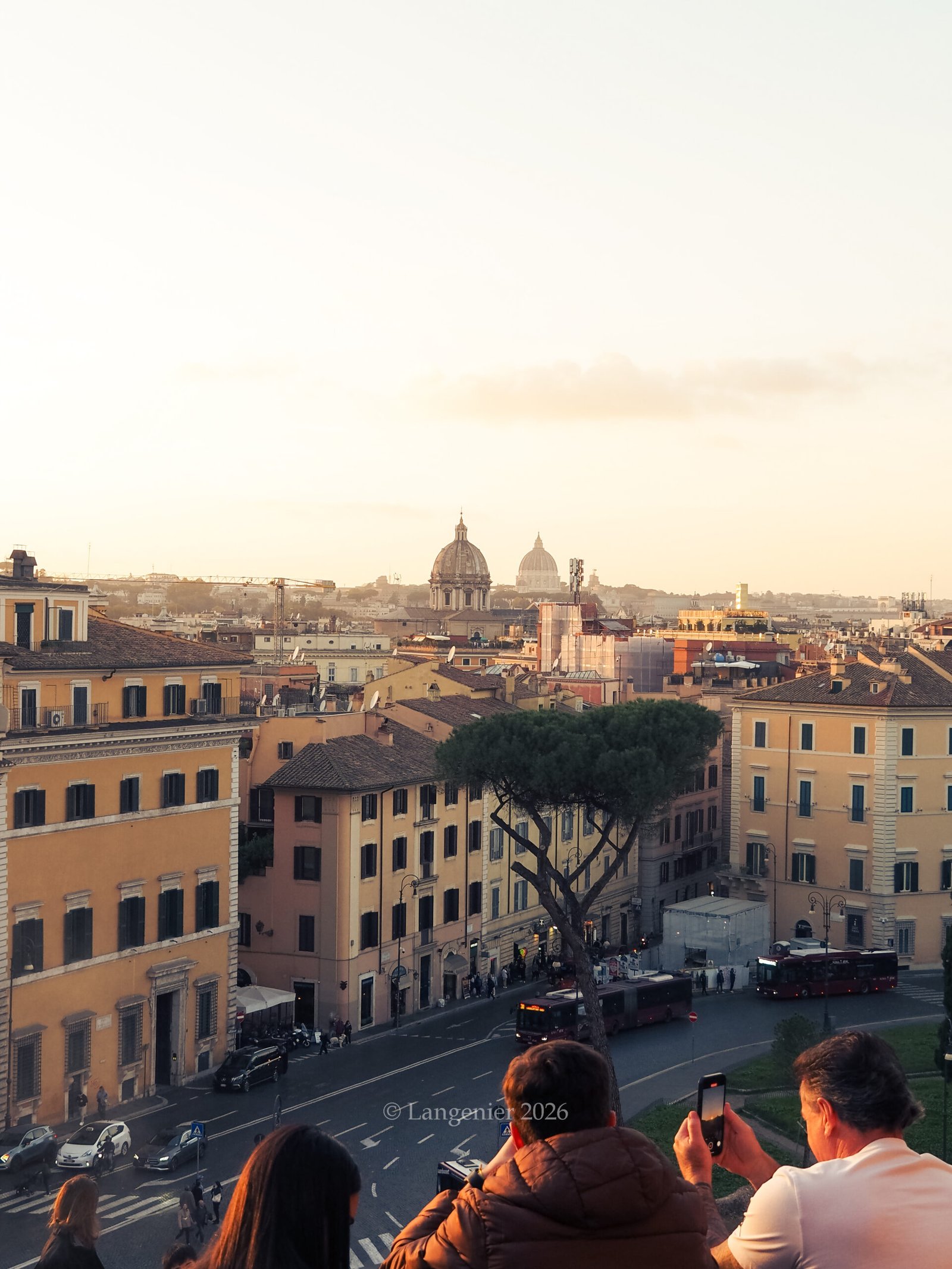 Visitors watching sunset from the terrace of the Basilica di Santa Maria in Aracoeli, overlooking Rome's rooftops toward the domes of St. Peter's Basilica