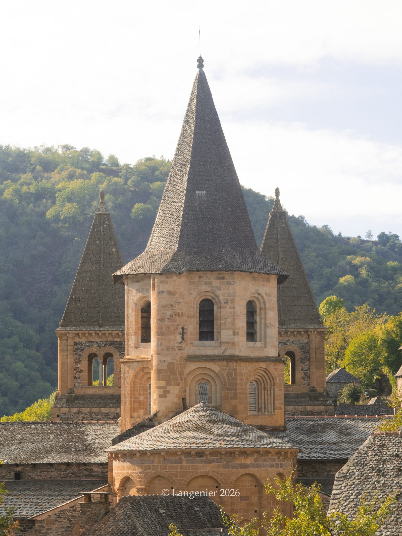 Conques Abbey in Aveyron, France, with its golden stone walls and slate roofs surrounded by autumn colours